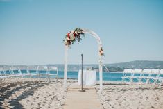 an outdoor ceremony setup on the beach with white chairs and flowers in the arch at the end of the aisle