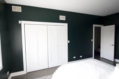 an empty bedroom with green walls and white closets on the far wall is a bed