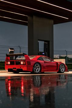 a red sports car parked in front of a gas station with its hood up and lights on