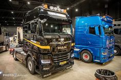 two semi trucks are parked in a warehouse with other vehicles around them and one is blue