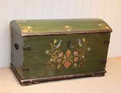 an old green painted chest with birds and flowers on the front, sitting against a white wall