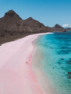 a pink beach with blue water and mountains in the background