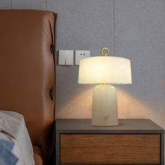 a nightstand with a lamp on top of it next to a brown chair and wall