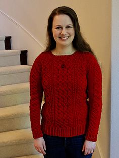 a woman standing in front of some stairs wearing a red cabled sweater and jeans