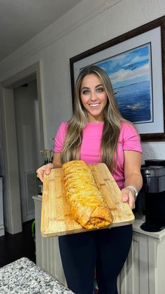 a woman holding a large loaf of bread on a cutting board