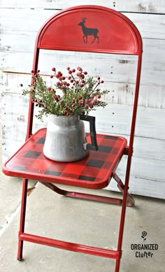 a red chair with a metal planter and flowers in it sitting on a checkered table