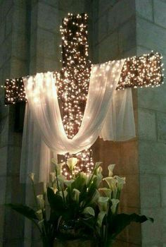 a cross decorated with lights and flowers in front of a wall mounted crucifix