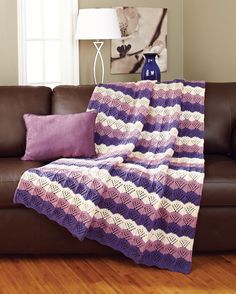 a purple and white crocheted blanket sitting on top of a couch next to a lamp