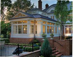 a large white house sitting next to a lush green tree filled park at dusk with the sun shining on it's windows