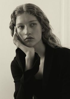 a black and white photo of a woman with her hand on her chin, looking at the camera