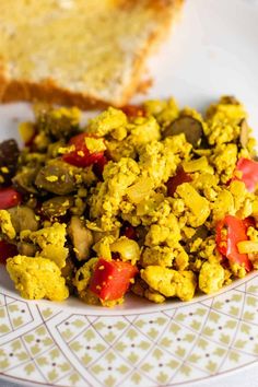 a white plate topped with scrambled eggs and tomatoes next to bread on top of a table