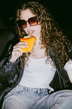 a woman sitting in a car eating an orange slice and drinking milk from a cup