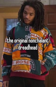 a man with dreadlocks standing in front of a door wearing a colorful sweater