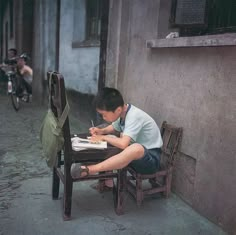 a young man sitting at a table writing on a piece of paper