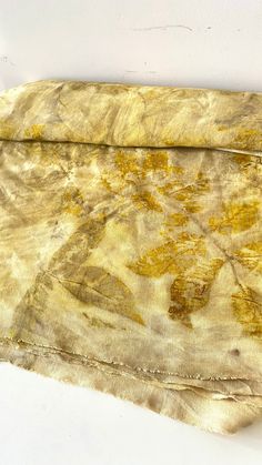 a piece of cloth with yellow and brown designs on it, sitting on a white surface