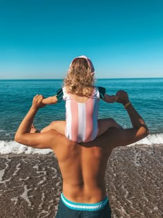 a man standing on top of a beach next to the ocean holding onto his hat