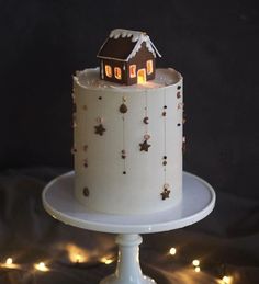 a white cake topped with a small house on top of a table covered in lights