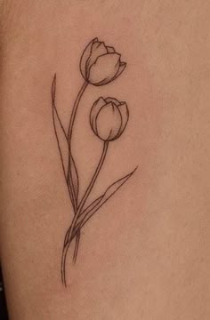 a small flower tattoo on the back of a woman's left thigh, with two tulips growing out of it