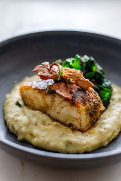 a piece of fish on top of mashed potatoes and broccoli in a bowl