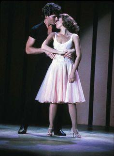 a man standing next to a woman in a white dress on a stage with his arm around her waist