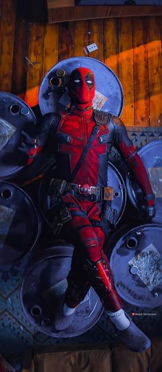 a man dressed as deadpool is sitting in front of some metal circles and looking at the camera