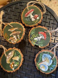 four handmade wood slices with mushrooms on them are sitting on a black tray, ready to be used as ornaments