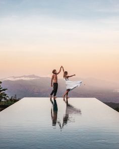 two people standing on the edge of a swimming pool with their arms in the air