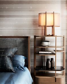 a bed with blue sheets and pillows next to a lamp on a wooden book shelf