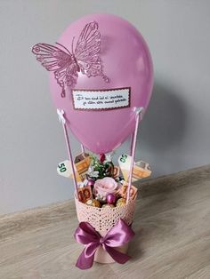 a pink balloon filled with lots of candies and sweets in a basket on top of a wooden table