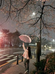 a woman is walking down the sidewalk with an umbrella in her hand at night time