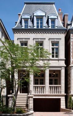 a large white building with two stories and a tree in front of the entrance to it