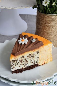 a piece of cheesecake on a plate next to a vase with flowers and greenery