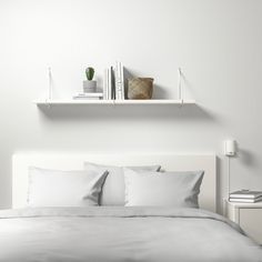 a bed with white sheets and pillows on top of it next to a book shelf