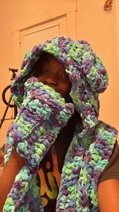 a woman is wearing a crocheted scarf and covering her face with one hand