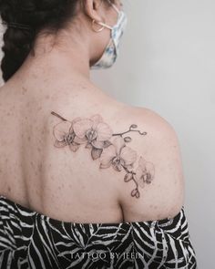 the back of a woman's shoulder with an orchid tattoo on her upper arm