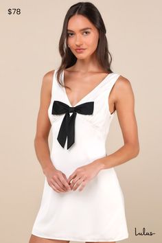 However you decide to style the Motel Faradiba Ivory Satin Sleeveless Bow Mini Dress, we know it'll be on trend! Sleek woven satin shapes this sleeveless dress that features a lightly gathered bodice, a flirty V-neck (and back), and wide tank straps. A high, empire-style waist tops a figure-skimming sheath silhouette that falls to a flirty mini hem. A darling black bow accents the front of this dress for the perfect coquette finish. Hidden side zipper. Fit: This garment fits true to size. Length: Mid-thigh. Size medium measures 31.25" from shoulder to hem. Bust: Works best for A to C cup sizes - consider sizing up for fuller bust. Waist: Fitted - very fitted at natural waist. Hip: Loosely Fitted. Undergarments: May be worn with a strapless bra, adhesive bra, petals, or no bra. Fabric: Fabr Spring Graduation Dress, White Wedding Guest Dresses, White Dress Fall, Nola Bachelorette, Short Mini Dresses, Bow Mini Dress, Short Cocktail Dresses, Dresses For Juniors, Cute Flirty