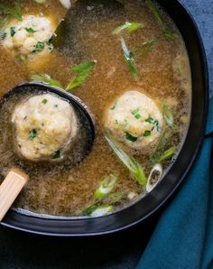 a pot filled with soup and dumplings on top of a blue cloth next to a wooden spoon