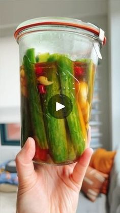 a person holding up a jar filled with pickles and other veggies in it