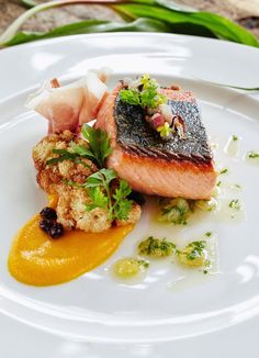 a white plate topped with fish and vegetables on top of sauce covered bread crumbs