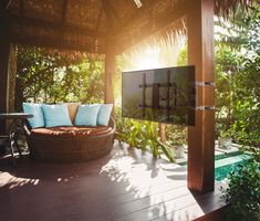 an outdoor patio area with wicker furniture and plants on the deck, surrounded by greenery