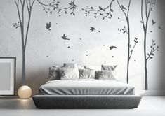 a white bed sitting under a tree with birds flying around it and two framed pictures on the wall