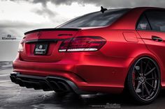 the rear end of a red car parked on top of a wet ground with dark clouds in the background