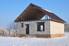 a small house under construction in the middle of winter with snow on the ground and blue sky