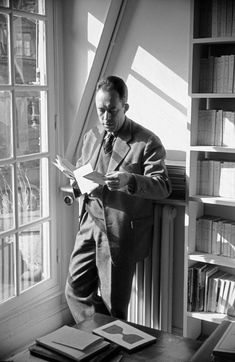 black and white photograph of man reading in front of window with bookshelf behind him