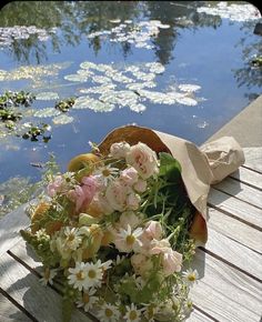 a bouquet of flowers sitting on top of a wooden bench next to a body of water