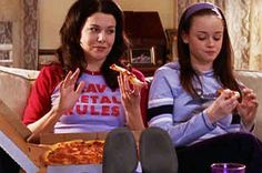 two women sitting on a couch eating pizza