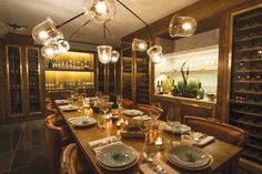 a dining room table is set with place settings and wine bottles on the shelves behind it