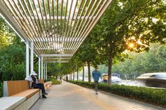 a person sitting on a bench under a pergolated area with trees and bushes