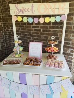 a table topped with lots of donuts on top of a white cake stand next to a brick wall