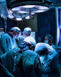 several doctors in scrubs and surgical gowns looking at something on the monitor screen